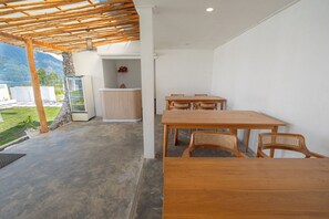 A covered patio area with a wooden table and chairs, a stone wall, and a small refrigerator. - Pulestis Glamping (Kintamani)