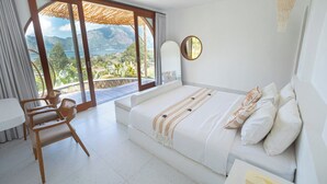 A bedroom with a bed, a desk, and a chair. There is a large window with a view of mountains and the sea. - Pulestis Glamping (Kintamani)