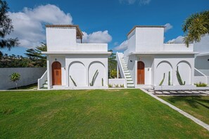 A modern two-story house with white walls and wooden doors, featuring a well-maintained lawn and a staircase leading to the upper level. - Pulestis Glamping (Kintamani)