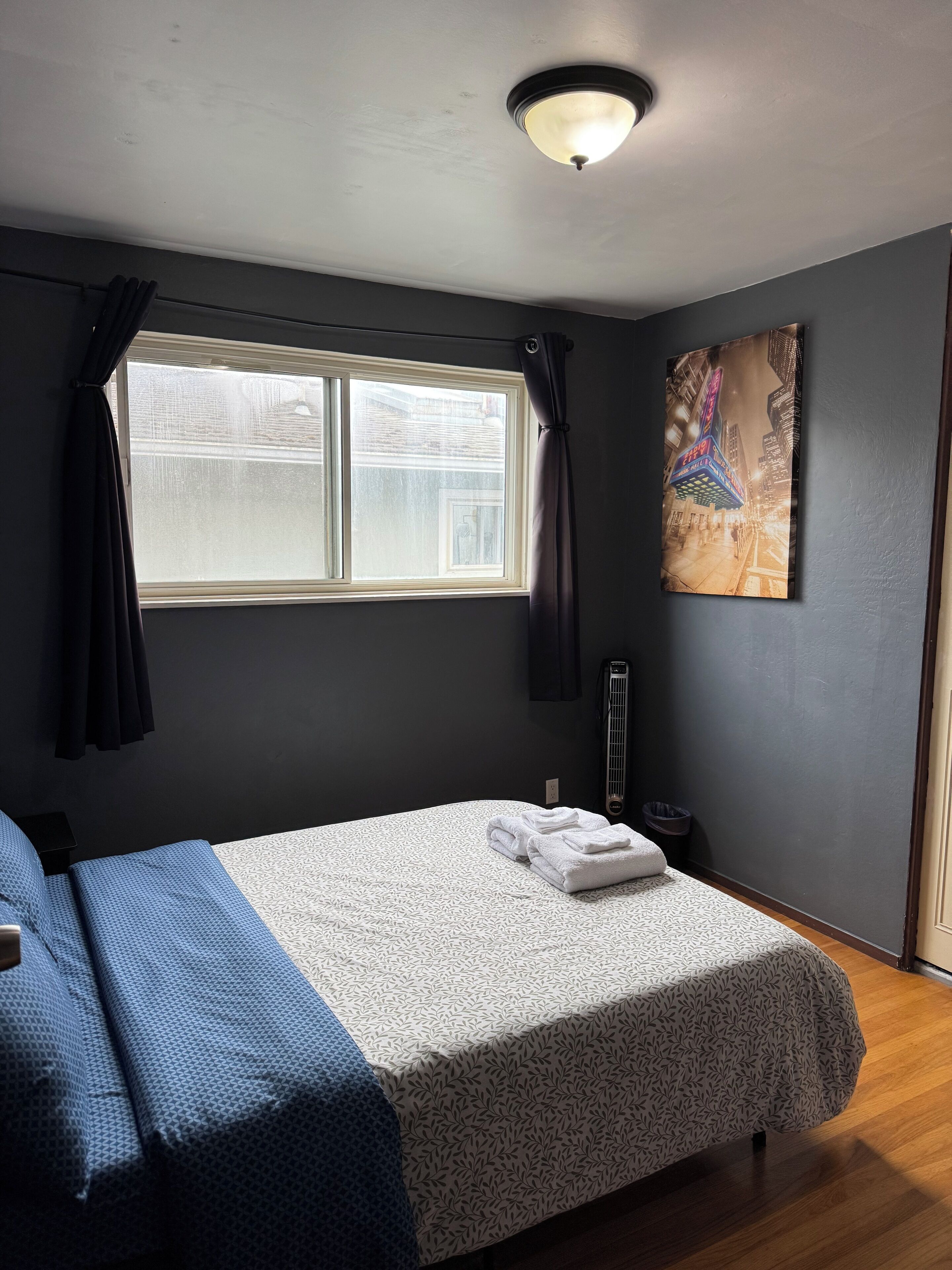 A bedroom with a bed, a window with curtains, a radiator, and a painting on the wall.