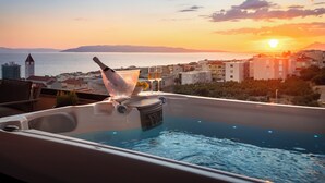 A hot tub with a bottle of champagne, overlooking a cityscape at sunset. - Seaview Apartment w/ Jacuzzi – Makarska (Makarska)