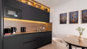 A modern kitchen with dark cabinetry, a built-in microwave, and a wooden countertop. There is a dining area with a round table and chairs, and three framed nautical-themed paintings on the wall. - Seaview Apartment w/ Jacuzzi – Makarska (Makarska)