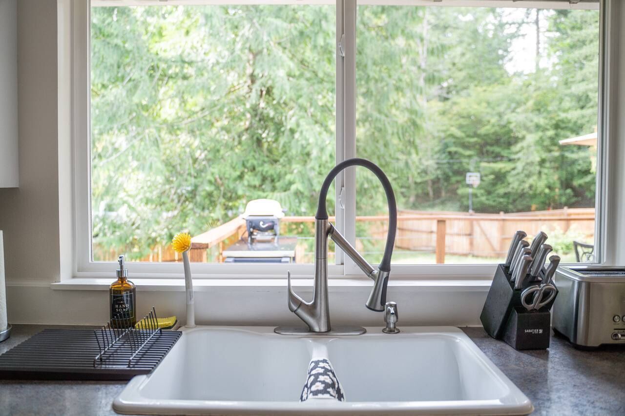A kitchen with a modern faucet, a window with a view of a backyard, and a knife block on the counter.