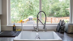 Una cocina con un grifo moderno, una ventana con vista a un jardín trasero y un bloque de cuchillos en la encimera.