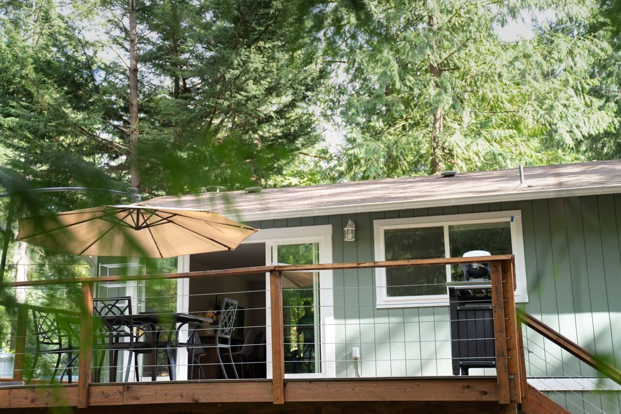 A covered deck with outdoor furniture, a grill, and a window overlooking a wooded area.