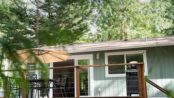 A covered deck with outdoor furniture, a grill, and a window overlooking a wooded area.