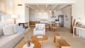 A modern living room with a sofa, coffee table, and chairs. There is a kitchen in the background with cabinets and appliances.