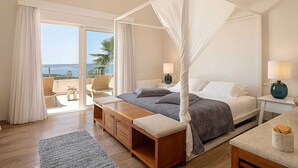 A bedroom with a canopy bed, a view of the sea, a balcony with a chair, and a wooden bench.