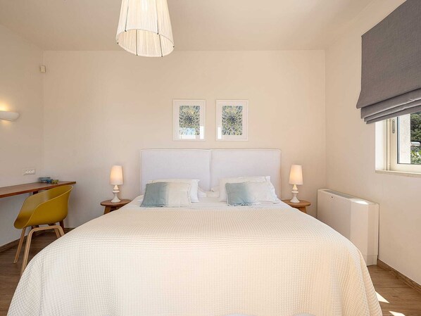 A bedroom with a large bed, two bedside tables with lamps, a chair, and a window with curtains.