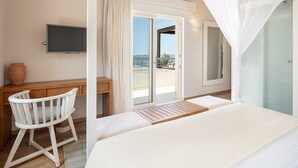 A bedroom with a bed, a desk, a chair, a television, and a balcony with a view of the sea.