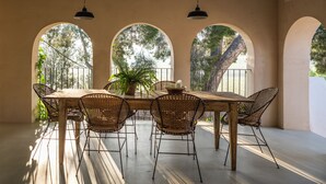 A dining area with a wooden table and wicker chairs, large arched windows, and hanging pendant lights. - Boutique Manor Farmhouse, pool & vineyard views, 35' Barcelona, 25' Sitges (Sant Pau d'Ordal)