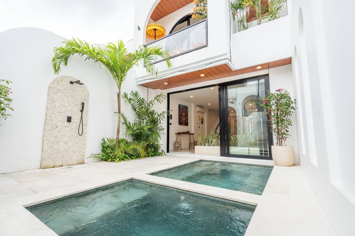 Ett modernt hus med en swimmingpool, en stenmur och en balkong med växter.