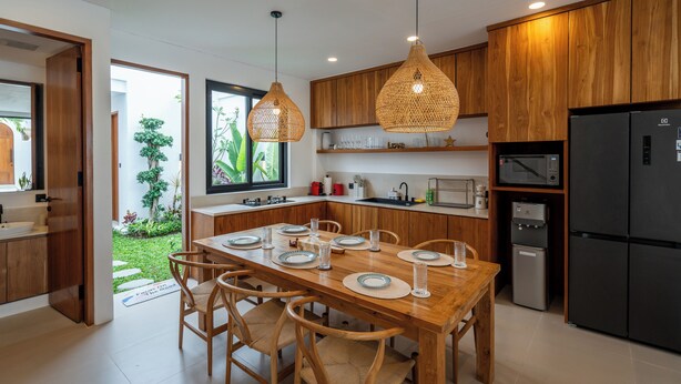 A modern kitchen with wooden cabinets, a dining table set for six, and a black refrigerator. - Amal Villas by Bali Bliss Properties (Canggu)
