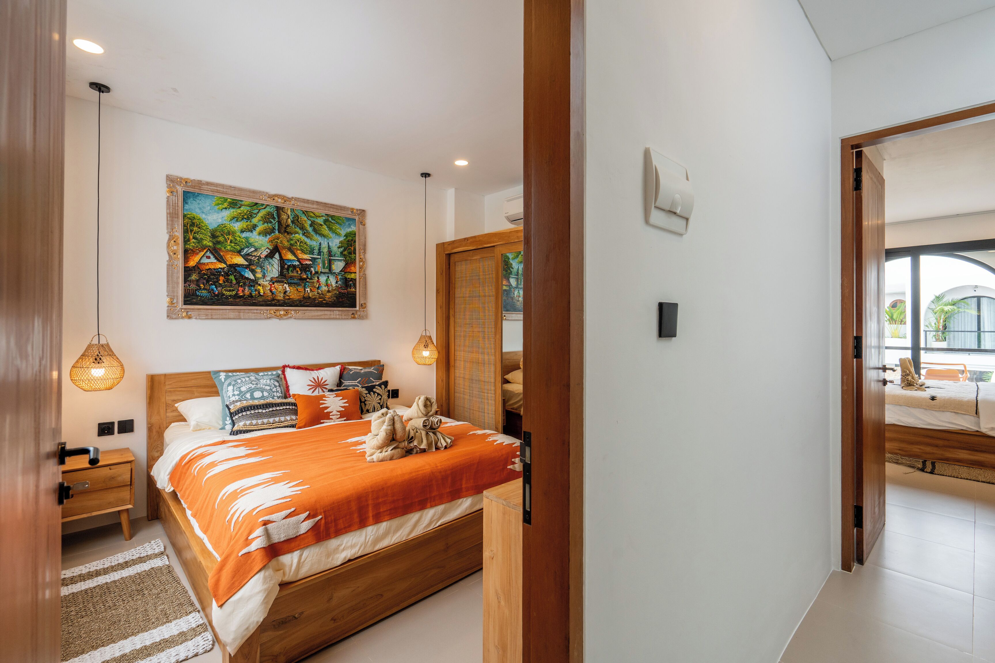 A bedroom with a wooden bed, a painting on the wall, and a view through an open door.