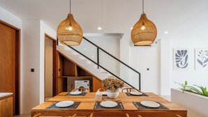 A dining area with a wooden table, six chairs, two hanging wicker lamps, and a staircase in the background. - Amal Villas by Bali Bliss Properties (Canggu)