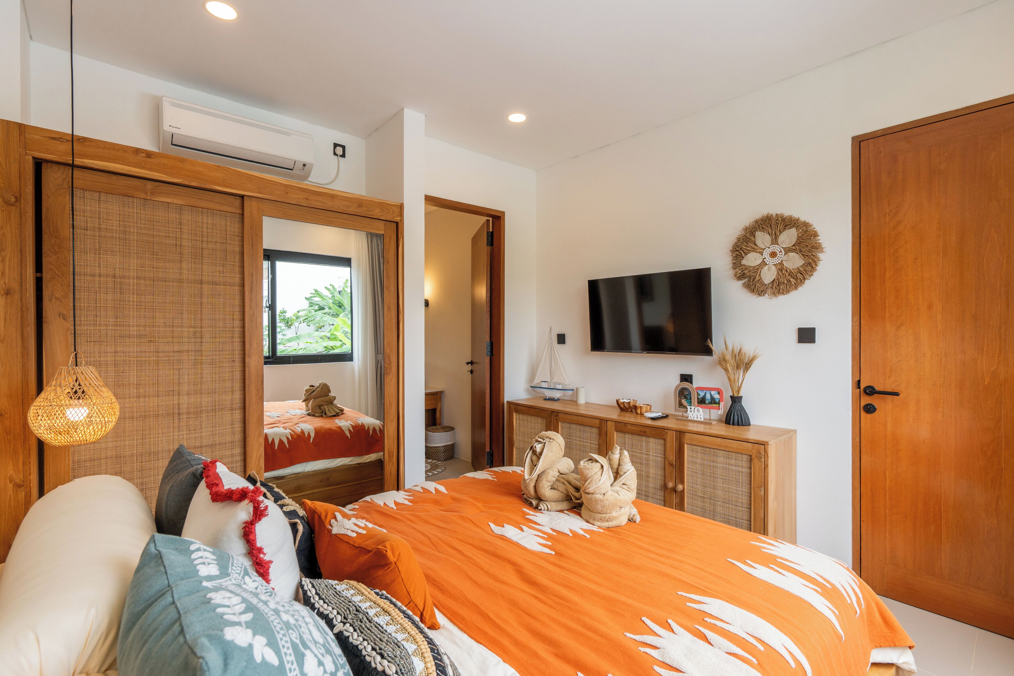 A bedroom with a large bed, a television, a wardrobe, and a window with a view of greenery.