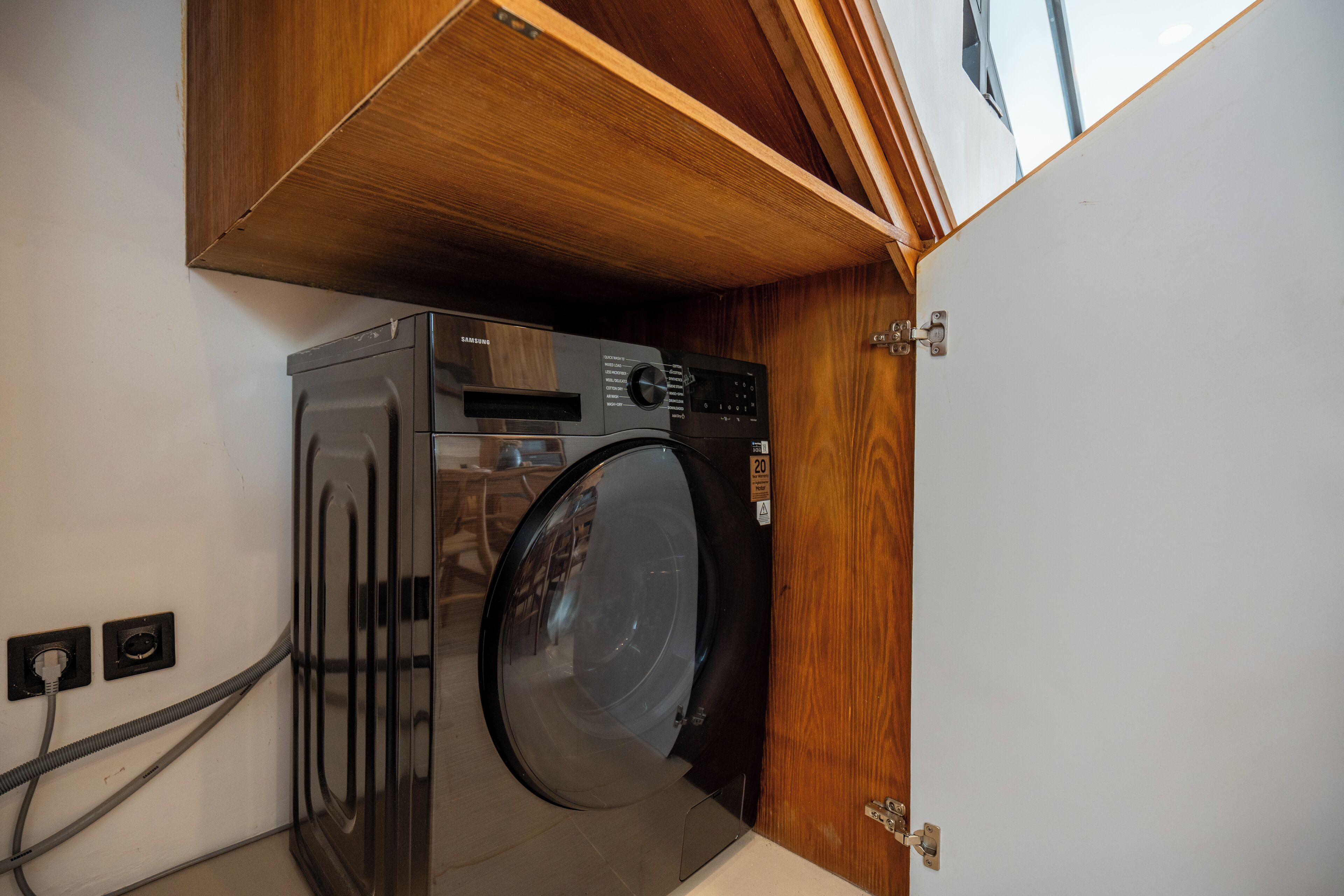 A compact laundry room with a front-loading washing machine and dryer, wooden cabinetry, and a visible electrical outlet.