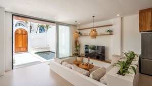 A modern living room with a sofa, TV, and a small dining table. - Amal Villas by Bali Bliss Properties (Canggu)