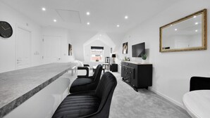 A modern kitchen with a marble countertop, black upholstered chairs, a black cabinet, and a large mirror on the wall.