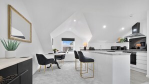 A modern kitchen with a central island, black bar stools, and a dining area with a white table and chairs.