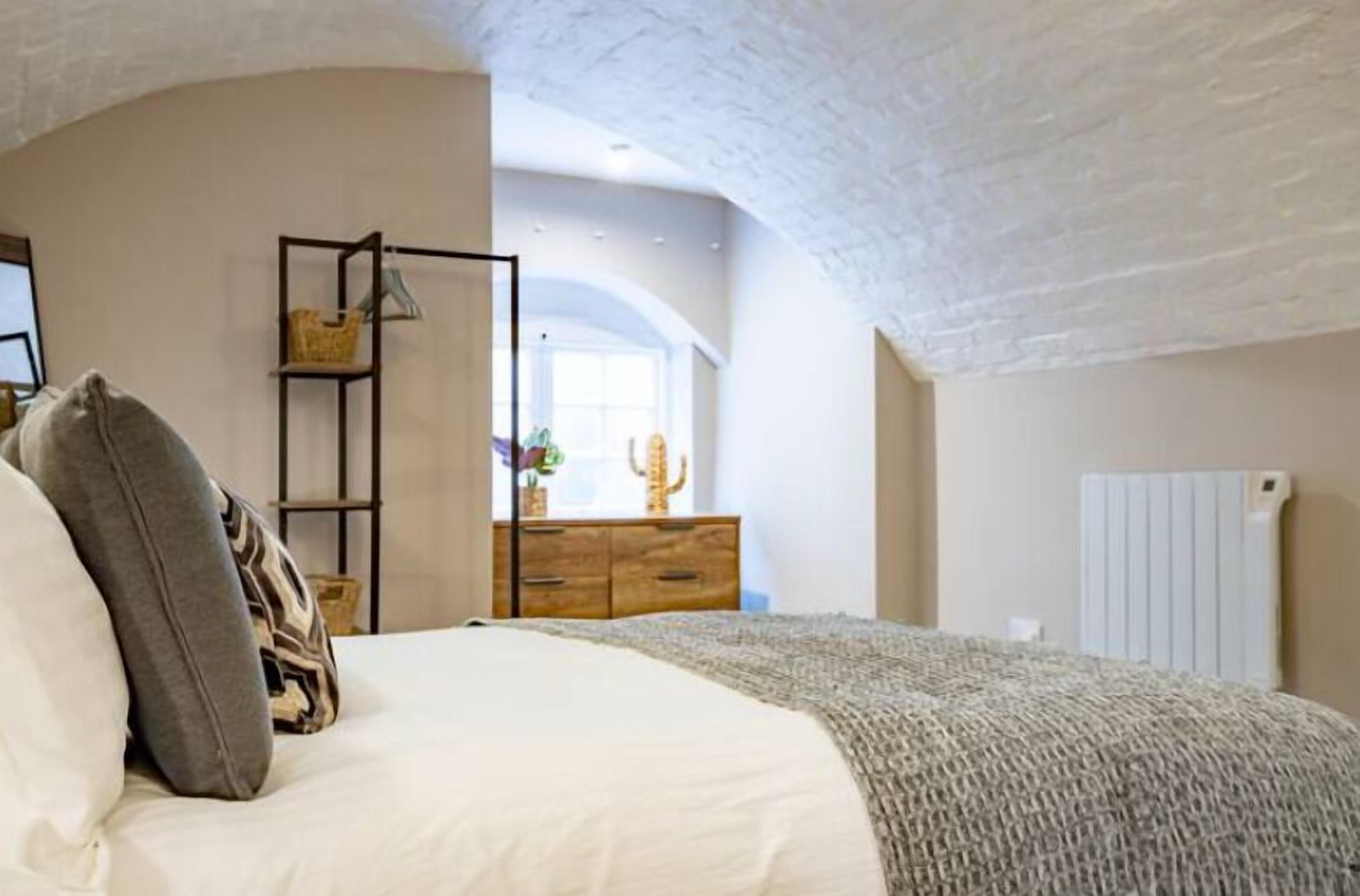 A bedroom with a bed, a wooden dresser, a shelf with baskets, and a radiator.