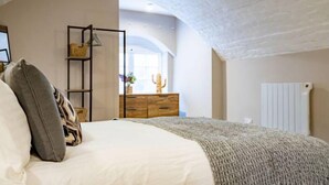 A bedroom with a bed, a wooden dresser, a shelf with baskets, and a radiator. - WhiskAwayHomes Shaw Street Apartment 2 (Worcestershire)