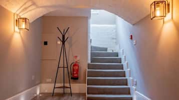 A staircase with a fire extinguisher and a ladder in a hallway with a white ceiling and wall sconces.