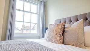 Ein ordentlich bezogenes Bett mit einer gemusterten Decke, einem gepolsterten Kopfteil und verzierten Kissen.