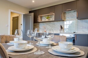 Una cocina moderna con muebles oscuros, un salpicadero de mármol y un comedor con mesa dispuesta para cuatro.