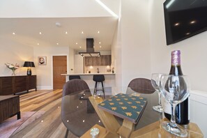 A modern living room with a glass dining table, a sofa, and a kitchen in the background. - WhiskAwayHomes Vinegar House No. 7 (Worcestershire)