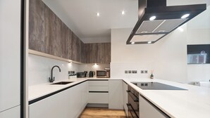 Une cuisine moderne avec des meubles blancs, un mur d’accent en bois, un plan de travail noir et des appareils électroménagers intégrés.