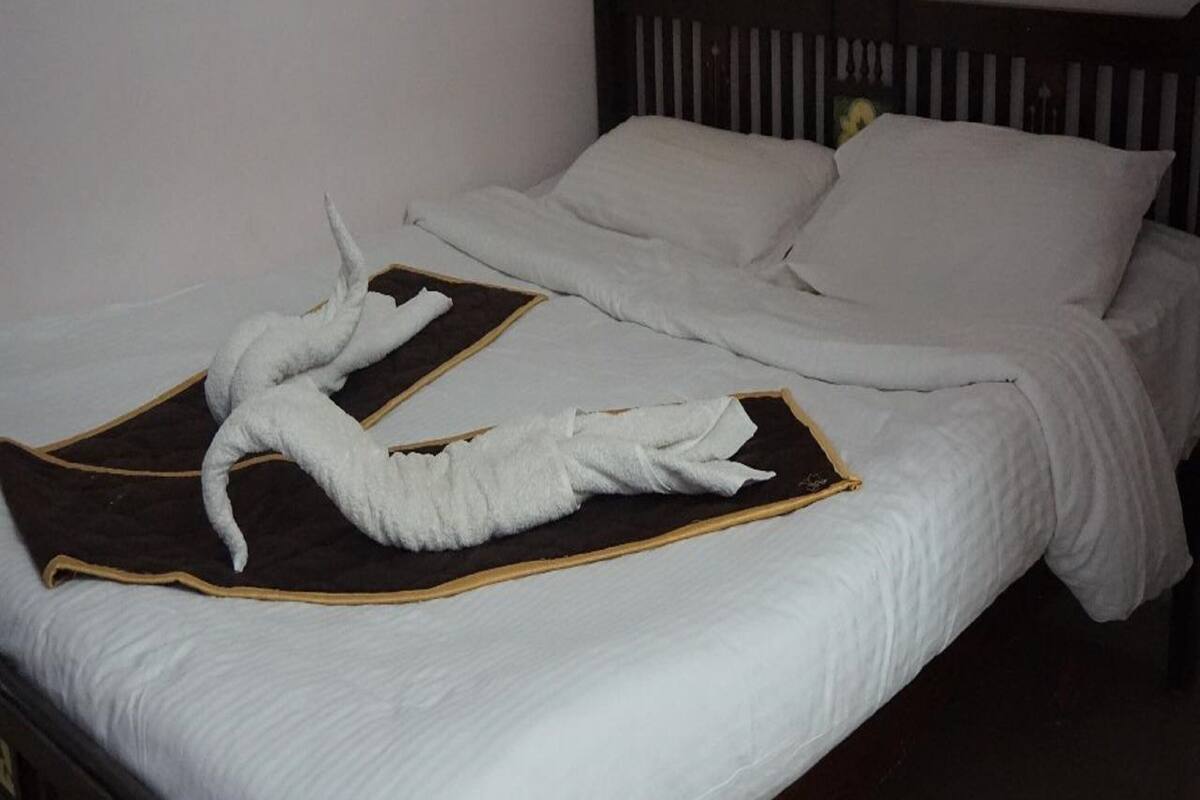 Un lit bien fait, avec du linge de lit blanc, une tête de lit sombre et une serviette posée sur le lit.