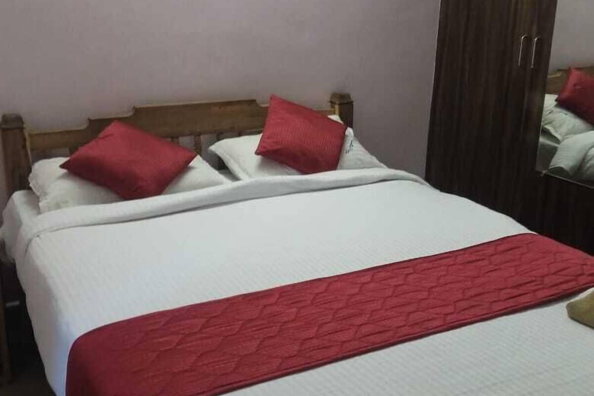 Un lit bien fait, avec une literie blanche et rouge, une tête de lit en bois et un coussin décoratif rouge.