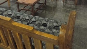 A living room with a wooden coffee table, four wooden chairs with patterned cushions, a television on a wooden stand, and a door with glass panels. - Vasantharaja Villa Ariyankuppam (Puducherry)