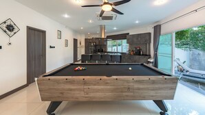Ein moderner Billardtisch mit Deckenventilator, Einbauleuchten und Blick auf eine Küche und einen Essbereich.