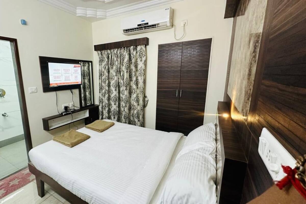 A hotel room with a bed, a TV mounted on the wall, a wardrobe, and a shower area.