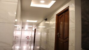 A corridor with reflective floors, recessed ceiling lights, and a wooden door on the right. - Vasantharaja Inn (Puducherry)