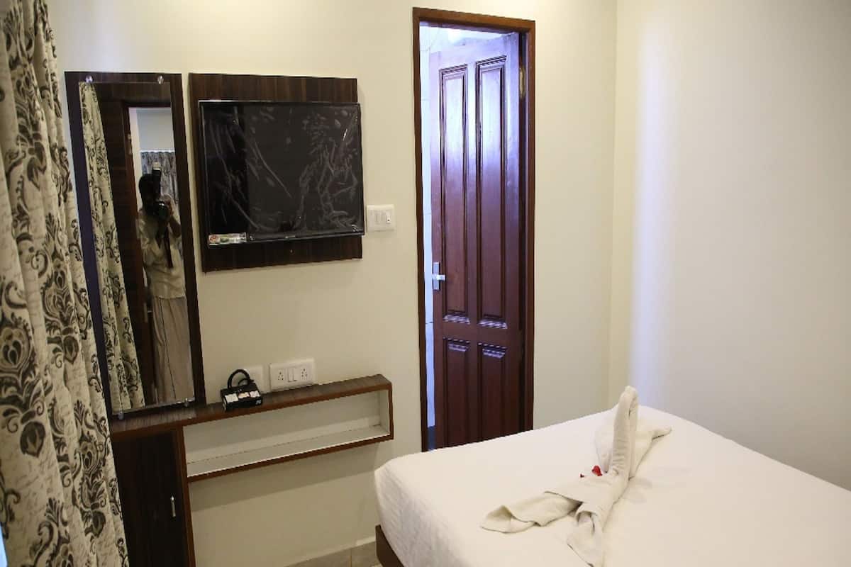 A hotel room with a bed, a TV mounted on the wall, a wooden door, and a mirror.