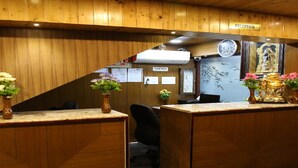 A reception area with wooden paneling, a reception desk, a clock, and a wall with a mural. - Vasantharaja Inn (Puducherry)