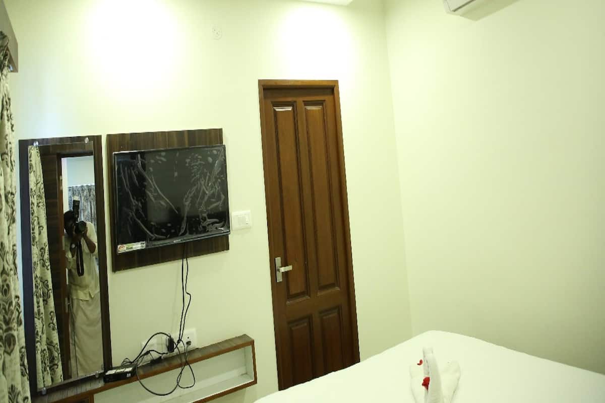 A hotel room with a bed, a wooden door, a ceiling fan, an air conditioner, a TV, and a mirror.