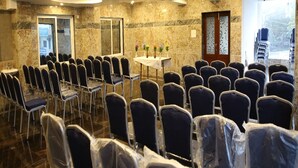 A conference room with rows of chairs, a table with water bottles, and a door with a view. - Vasantharaja Inn (Puducherry)