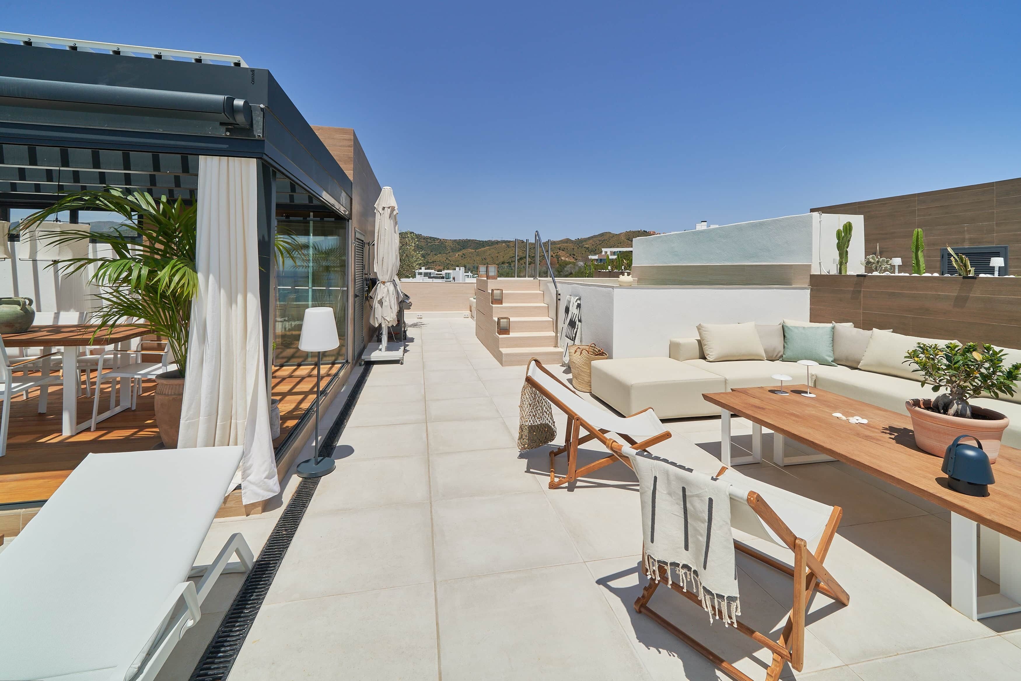 Eine Dachterrasse mit einer modernen Außenlounge, einer Treppe und Blick auf die umliegende Landschaft.