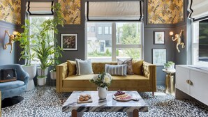 A cozy living room with a sofa, a coffee table with snacks, and a large window with a view of the outside.
