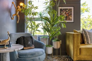 A room with a blue armchair, a yellow sofa, a table with a bag, and potted plants. - Colorful 4BR w/ Artful Design, Dining & Easy Access to Broadway | Bloom House (Nashville)