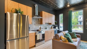 A modern kitchen with stainless steel appliances, wooden cabinets, and a large window offering a view of the outside.