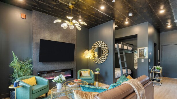 A modern living room with a flat-screen TV, a fireplace, a green armchair, a brown sofa, and a decorative mirror.