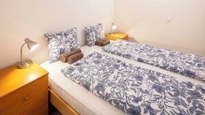 Et dobbeltværelse med to senge, hver med dyne med blomstermønster, en sengetavle, en lampe og en skuffe.