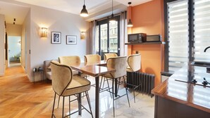A modern dining area with a wooden table and chairs, a kitchen area with a microwave, and a view through large windows. - Superb Apartement 2 Bedrooms Center of Paris (Paris)
