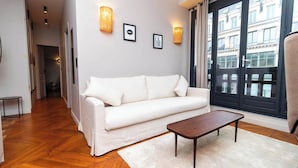 A modern living room with a white sofa, a wooden coffee table, and a view of a building through a large window. - Superb Apartement 2 Bedrooms Center of Paris (Paris)