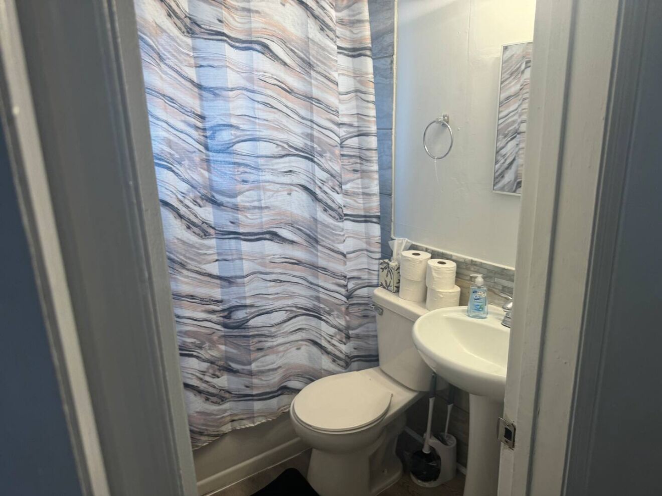 Een badkamer met een douchegordijn met marmerprint, een toilet en een wastafel met toiletartikelen.